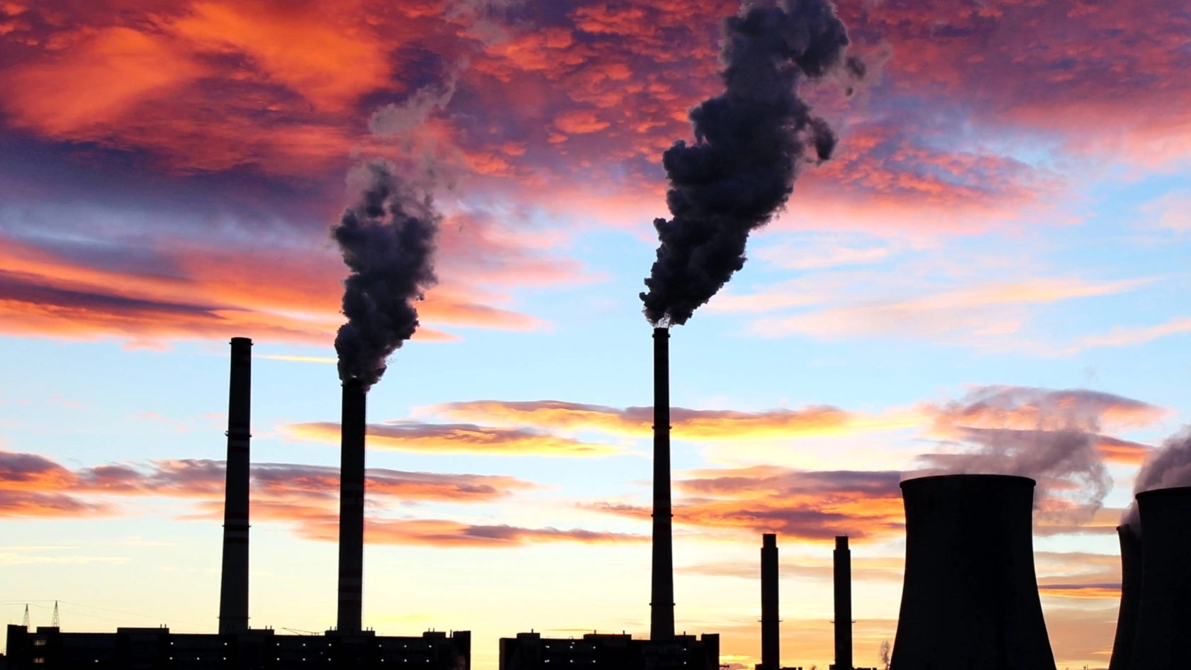 Rauchende Schlote eines Kraftwerks vor einem Sonnenuntergang.